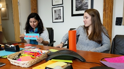 Two CAST interns working together with paper materials at a large table