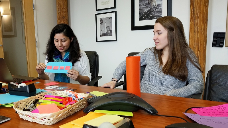 Two CAST interns working together with paper materials at a large table