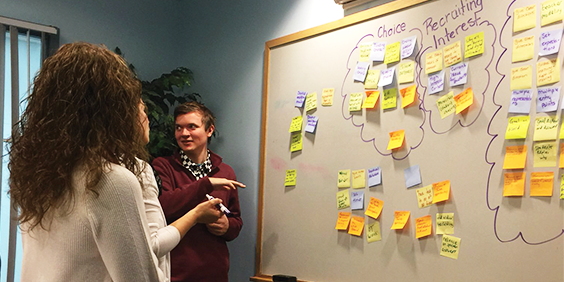 New Hampshire educators collaborating around a whiteboard with sticky notes on it