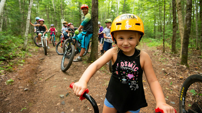 Photo of a group of children bike riding in the woods with adults