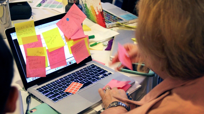 Photo of NH educators working together at a laptop computer covered in paper sticky notes