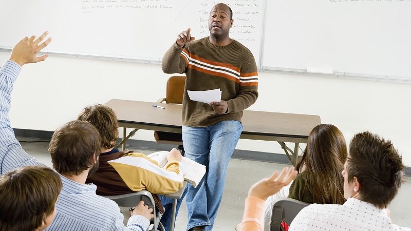 An educator at the front of a classroom of adults, calling on participants to speak