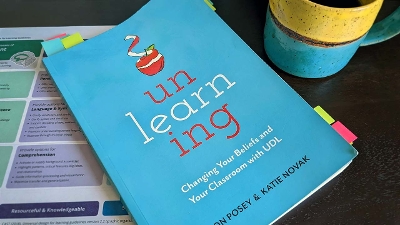 A well-loved copy of Unlearning with sticky notes, a mug of coffee, and the UDL Guidelines in the background