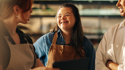 Photo of a woman with Down syndrome smiling and speaking to colleagues at a grocery store