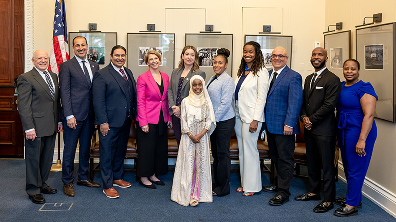  A young girl in a white headscarf and dress stands in the middle of the adults smiling as well