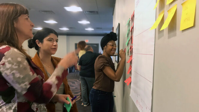 Photo of two adult women engaged in discussion pointing at a wall with sticky notes and chart paper. A woman in the background is smiling and writing on a sticky note on the wall., Illustration of a series of media representing varied ways of feeling, seeing and hearing content., Center on Inclusive Technology & Education Systems (CITES) logo, CAST mark, Various icons representing learning about UDL, Three CAST UDL Credentials badges