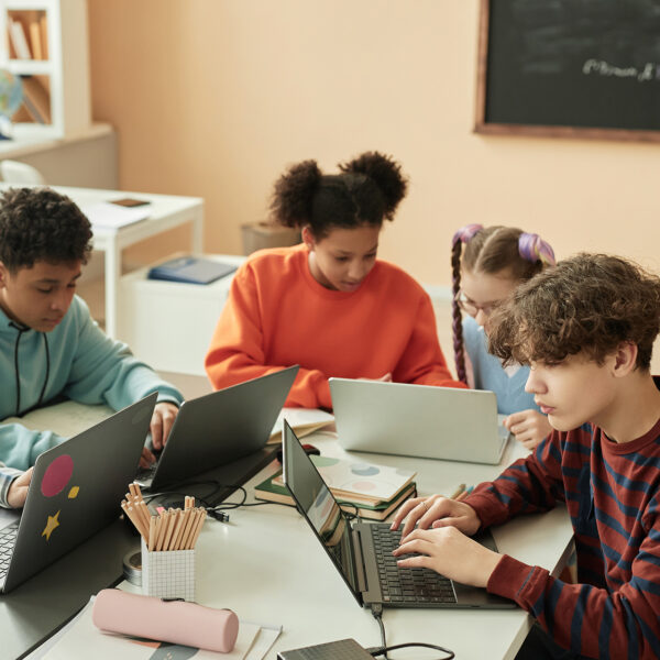 Four students sitting at a table in a classroom, using laptops.