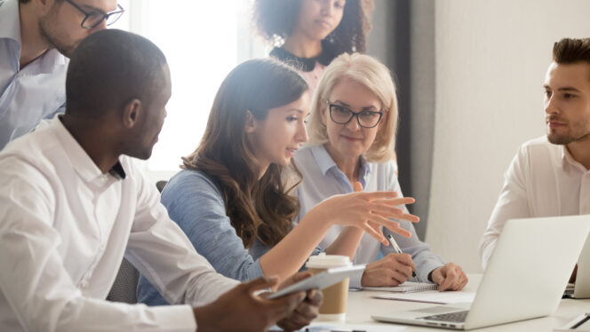 Young female mentor leader coach teaching employees group analyzing online project explaining business strategy speaking training diverse corporate team with laptop using computer at office meeting.