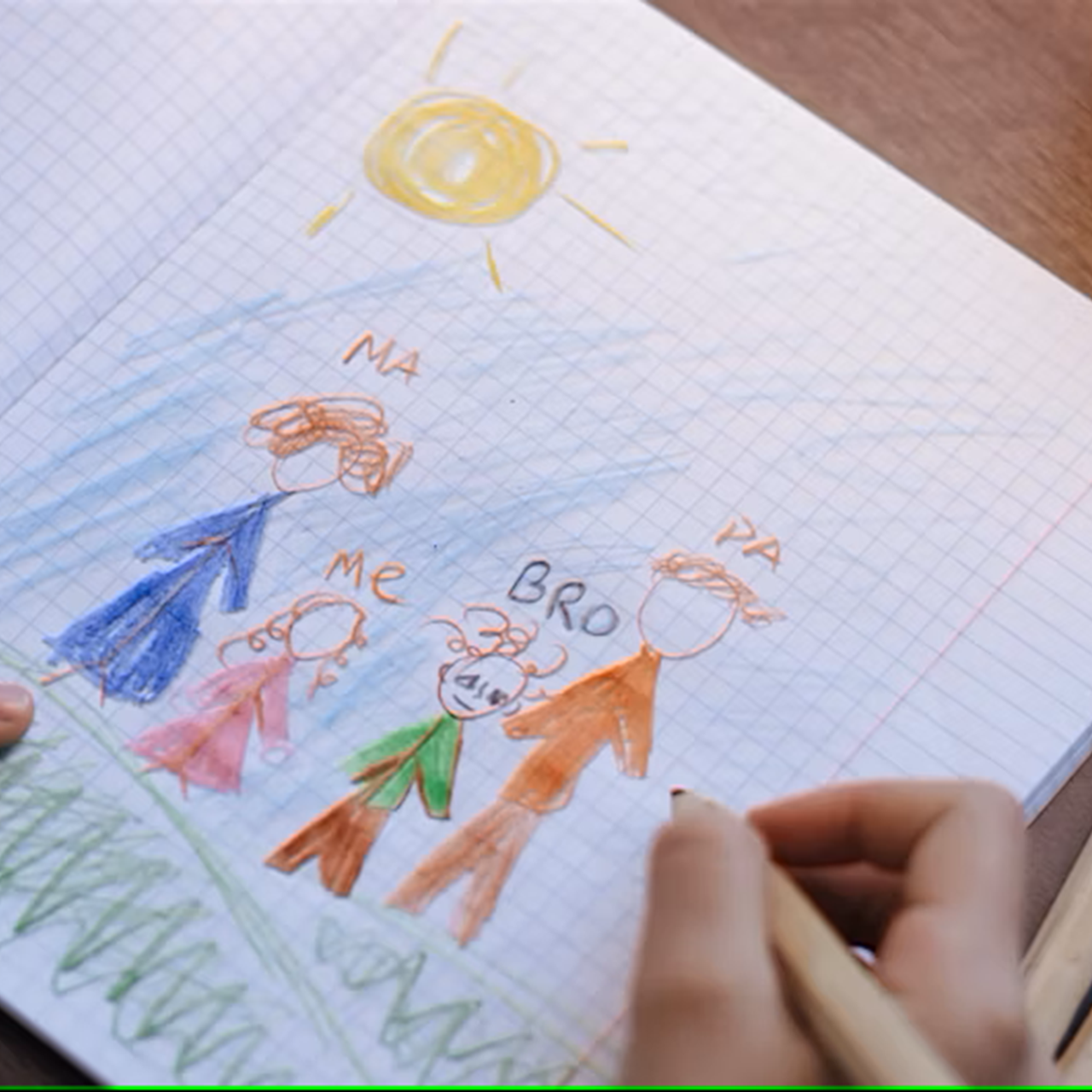 Photo of a child's hand drawing a colorful picture of their family in a notebook.