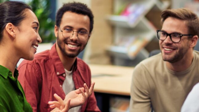 three young adult people sitting, talking, and smiles