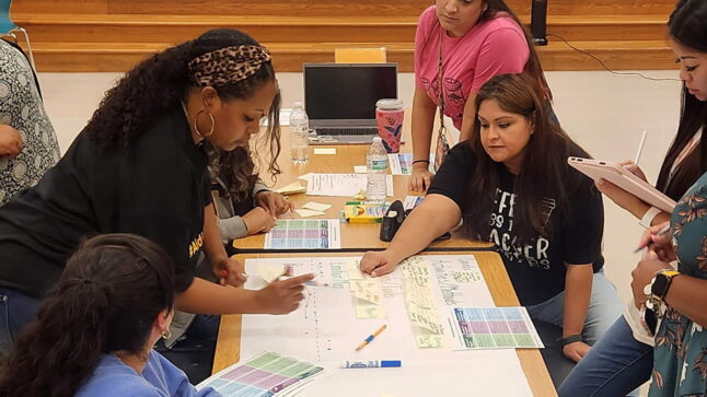 teachers gathered at a long table to work on a paper journey map using the UDL Guidelines, markers, and sticky notes.