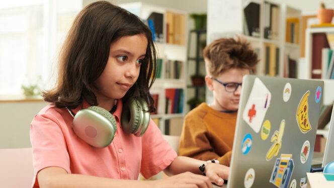 Kids in a classroom using sticker-covered laptops and headphones.