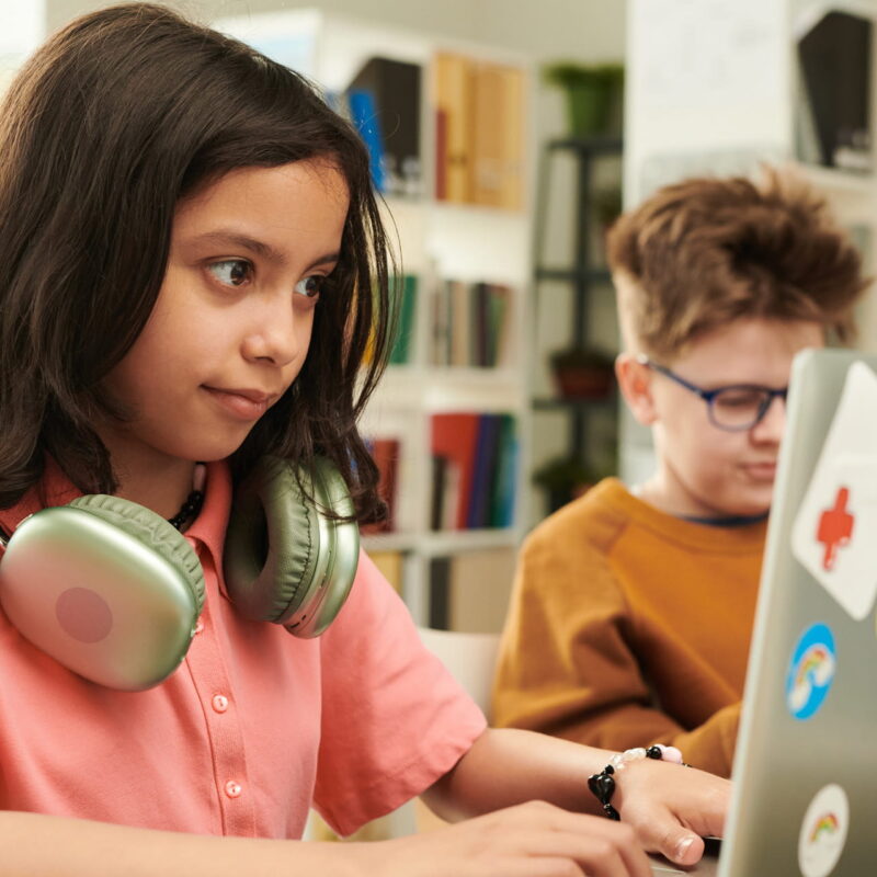 Kids in a classroom using sticker-covered laptops and headphones.